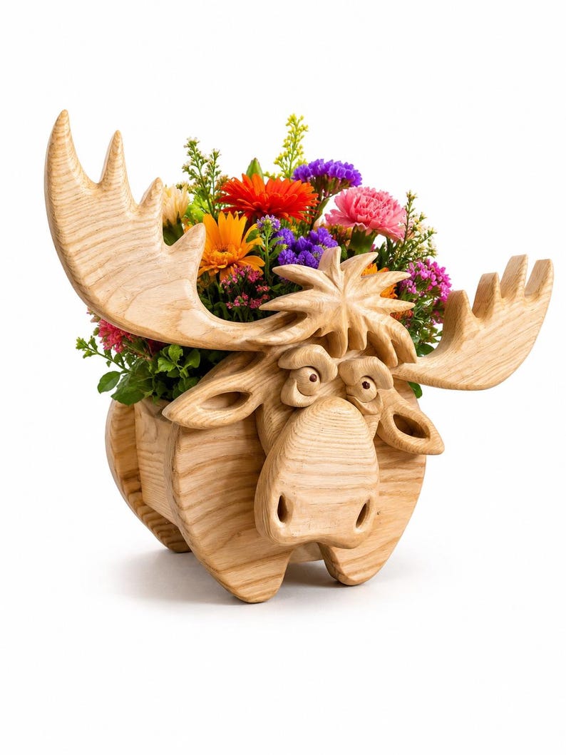 May include: A wooden moose planter with a carved face, antlers, and body. The planter is filled with a variety of colorful flowers, including orange, red, purple, and pink blooms. The moose is made of light-colored wood.