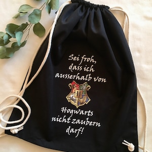 Könnte beinhalten: Schwarze Kordelzugtasche mit weißem Text und dem Hogwarts-Wappen. Der Text lautet "Sei froh, dass ich ausserhalb von Hogwarts nicht zaubern darf!"