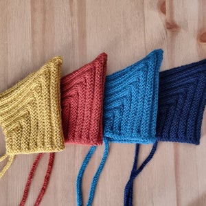 Puede incluir: Cuatro gorros de punto para bebé en diferentes colores: amarillo mostaza, naranja óxido, azul turquesa y azul marino. Cada gorro tiene una larga corbata que se puede atar debajo de la barbilla.