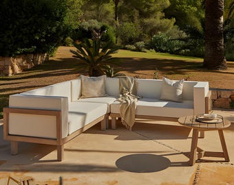 May include: A white sectional sofa with a wooden frame and white cushions. The sofa is set on a patio with a small round wooden table and a throw blanket.