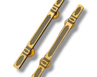 May include: A pair of gold door handles with black accents. The handles are long and rectangular with a decorative design.