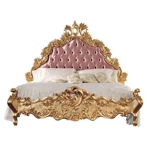 May include: A gold-leafed, ornate bed frame with a tufted pink headboard. The bed is made of wood and has intricate carvings. The bed is covered in white linens and pillows.