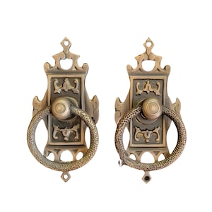 Könnte beinhalten: Zwei verzierte Türklinken aus Messing mit einem Ringgriff. Die Griffe haben ein dekoratives Design mit filigranen Details.