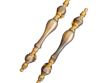 Pode incluir: Duas maçanetas de porta de ouro antigo com acabamento escovado. As maçanetas têm um design decorativo com uma parte superior arredondada e um corpo longo e delgado.