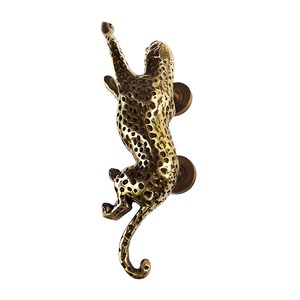 May include: A brass door knocker shaped like a leopard, with a detailed spotted pattern. The leopard is depicted in a climbing pose, with its tail curled around its body.
