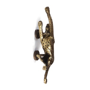 May include: A gold-toned brass door knocker shaped like a cheetah, with a spotted pattern, reaching up with its front paws.