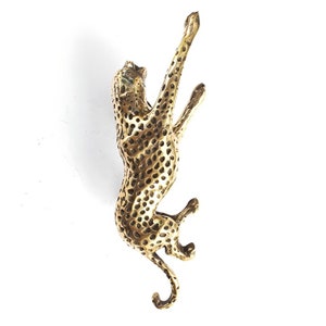 May include: A gold-colored metal sculpture of a cheetah, with a spotted pattern, climbing upwards. The sculpture is detailed and realistic.