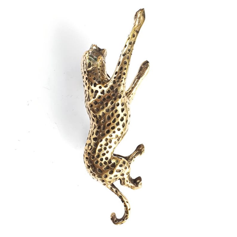 May include: A gold-colored metal sculpture of a cheetah, with a spotted pattern, climbing upwards. The sculpture is detailed and realistic.