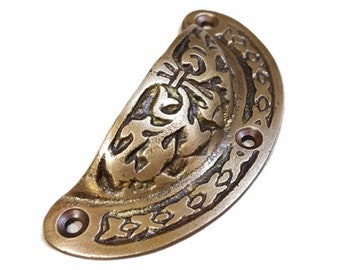 Puede incluir: Un tirador de cajón de latón con un diseño floral ornamentado. El tirador tiene dos agujeros para el montaje.