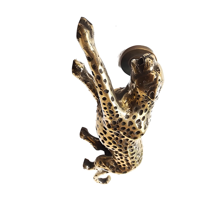 May include: A gold-toned metal door knocker shaped like a cheetah. The cheetah is in a leaping pose with its mouth open.