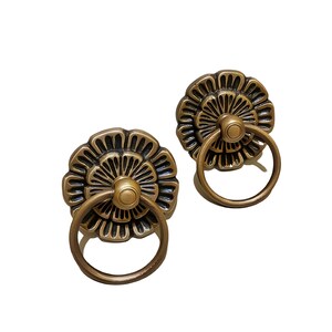 May include: Two antique brass cabinet knobs with a floral design and a ring pull.