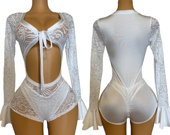 Puede incluir: Body blanco de encaje con mangas largas y escote pronunciado. El body tiene un corte en la cintura y un dobladillo con volantes.