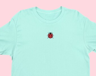 May include: A light blue t-shirt with a small embroidered ladybug in the center.