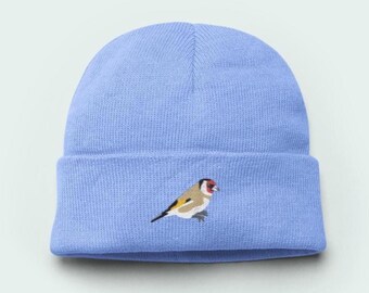May include: A light blue beanie hat with a folded brim. The hat features an embroidered goldfinch bird design on the front. The bird has a red face, a white and tan body, and yellow and black wings.