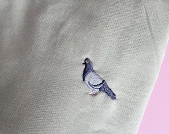 May include: A light gray t-shirt with an embroidered dove in the center.