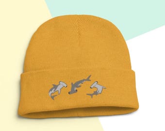 May include: A mustard yellow beanie with an embroidered design of three hammerhead sharks.