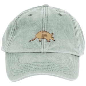 May include: A light green baseball cap with a brown armadillo embroidered on the front. The cap has a curved brim and an adjustable strap at the back. The armadillo is depicted in a side profile.
