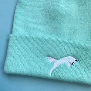 May include: A light blue knitted beanie with a white embroidered fox design.