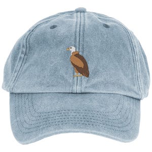 Könnte beinhalten: Eine hellblaue Baseballkappe aus Denim mit einer gestickten Grafik eines braun-weißen Adlers auf dem vorderen Mittelteil. Die Kappe verfügt über einen gebogenen Schirm, sichtbare Nähte und einen Knopf an der Oberseite der sechsteiligen Krone.