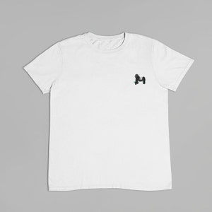 May include: A white t-shirt with a small black and green graphic of a monkey on the left chest.