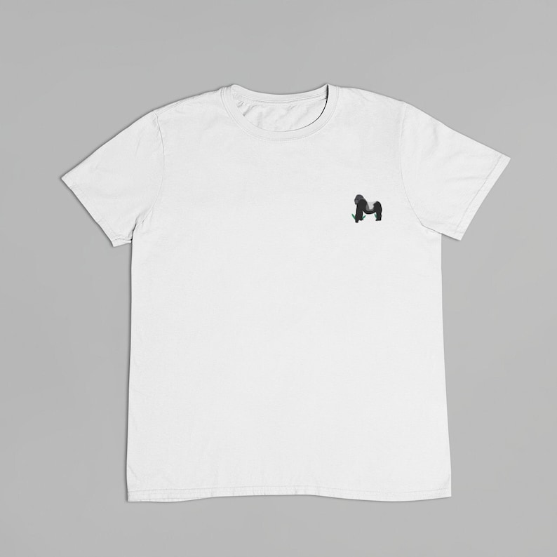 May include: A white t-shirt with a small black and green graphic of a monkey on the left chest.
