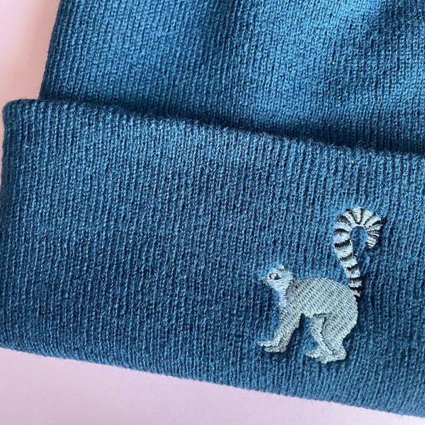 May include: A dark blue knitted beanie with a light blue embroidered lemur design.