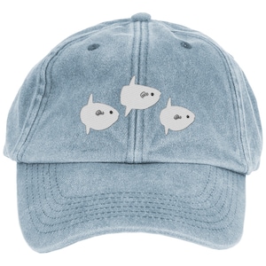 Könnte beinhalten: Hellblaue Jeans-Baseballkappe mit drei Cartoon-Mondfischen. Die Mondfische sind weiß mit schwarzen Augen und einem kleinen Mund. Die Kappe hat einen gebogenen Schirm und einen verstellbaren Riemen.