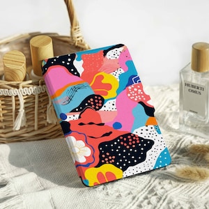 Könnte beinhalten: Eine E-Reader-Hülle mit einem bunten, abstrakten Design. Das Design zeigt rosa, blaue, gelbe, rote und schwarze Formen und Muster.