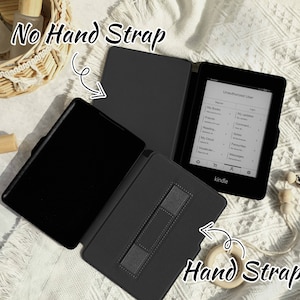 May include: Two black Kindle e-reader cases, one with a hand strap and one without. The case with the hand strap has a black strap with a gray textured surface. The case without the hand strap is open and shows the black interior.