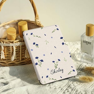 May include: A white e-reader cover with a floral pattern in blue and green. The cover has the name "Shirley" printed on it.