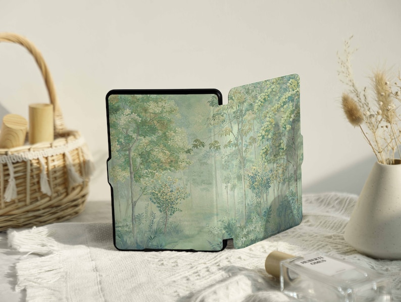May include: A black e-reader with a forest scene cover. The cover is a watercolor painting of trees and foliage in shades of green, blue, and white.