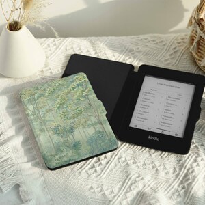 May include: A black Kindle e-reader with a forest scene cover. The e-reader is open to a page with a list of books. The cover is a green and white pattern of trees.