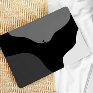 May include: A laptop computer with a black and gray abstract design on the cover. The laptop is lying on a woven surface.