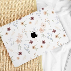 Könnte beinhalten: Ein weißer Laptop mit einem floralen Design auf dem Deckel. Die Blumen sind in Rosa-, Blau- und Brauntönen gehalten. Der Laptop steht auf einer gewebten Oberfläche.