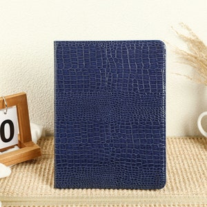 May include: A dark blue faux leather notebook with a crocodile skin pattern.