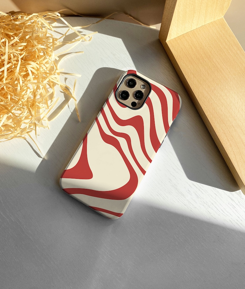 May include: A white phone case with a red and white abstract swirl pattern. The case has a cutout for the camera lens.