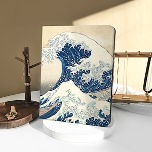 Könnte beinhalten: Ein blauer und weißer illustrierter Notizbuchumschlag mit einer großen Welle, die gegen einen Berg kracht. Die Welle ist im traditionellen japanischen Stil dargestellt.