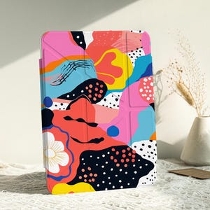 Könnte beinhalten: Eine Tablethülle mit geometrischem Muster in Pink, Blau, Gelb und Schwarz auf weißem Hintergrund.