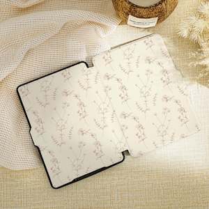 Puede incluir: Una funda para lector electrónico con estampado floral blanco y negro con un delicado diseño floral.