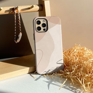 Könnte beinhalten: Eine beige und weiße Handyhülle mit abstraktem Design. Die Hülle hat eine schwarze Kamera-Erhebung mit drei Objektiven.