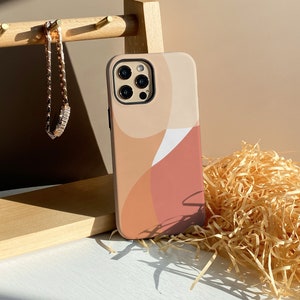 May include: A beige phone case featuring an abstract design in peach, tan, and white. A wooden jewellery holder with a gold chain bracelet is next to the case. Decorative straw is in the background.