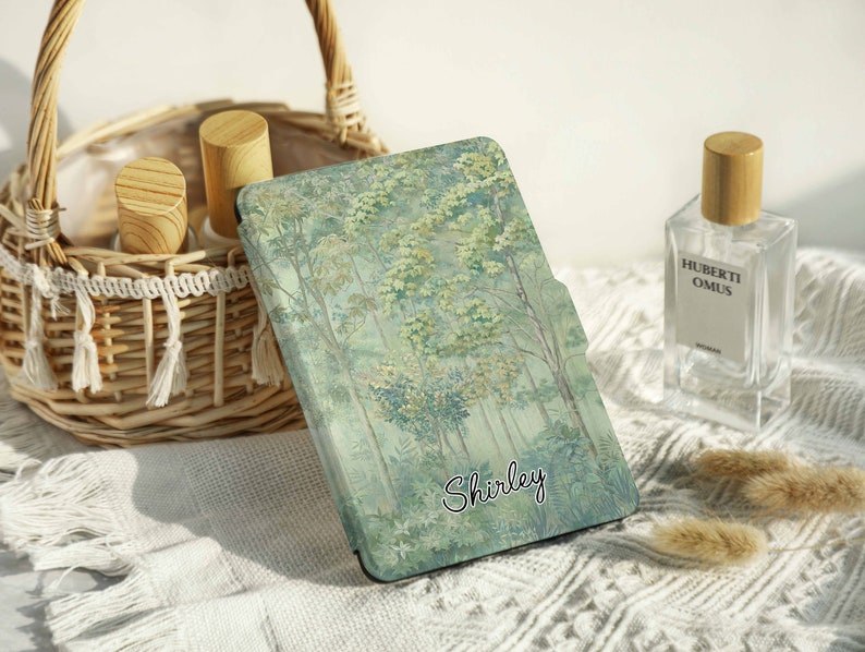 May include: A green and blue patterned e-reader case with the name "Shirley" printed on it. The case is lying on a white crocheted surface.