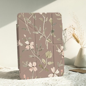 Può includere: Una custodia per tablet marrone con un motivo floreale con fiori rosa e foglie verdi. La custodia ha un design geometrico con una superficie testurizzata.