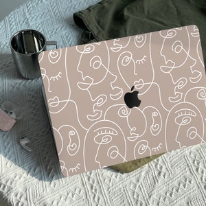 Könnte beinhalten: Ein Laptop mit einer beigefarbenen Haut, die mit einem weißen Linienkunstdesign aus abstrakten Gesichtern verziert ist. Das Design ist ein sich wiederholendes Muster von Gesichtern mit Augen, Nasen und Mündern.