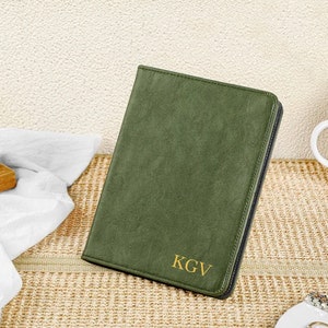 Könnte beinhalten: Eine grüne Lederhülle mit einem goldenen Monogramm "KGV" für ein Tablet oder einen E-Reader.