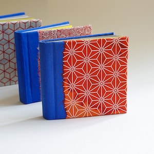 May include: Three small, blue-covered books with different patterned covers. The covers are red and white with geometric designs.