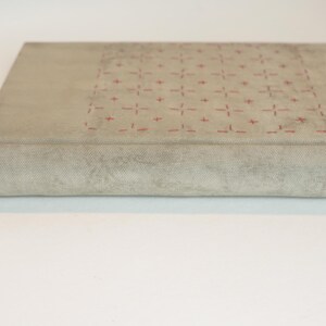 May include: A rectangular, light gray book with a textured cover. The top surface features a grid pattern of small red cross-like designs. The spine is rounded, and the book appears to be closed.