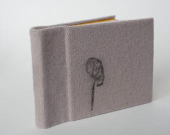 Puede incluir: Un pequeño libro de tapa gris de lino con un diseño floral negro en la portada.