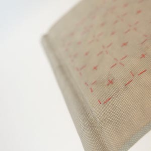 May include: Close-up of a book with a light gray cover featuring a grid pattern of red dashes. The book's pages are white, and the spine has a yellow accent.