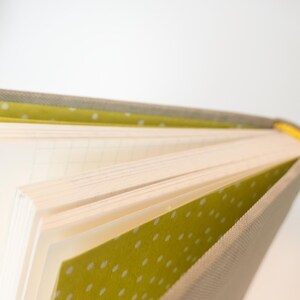 May include: Open notebook with lined pages. The cover is a light gray fabric with a yellow and white polka dot pattern on the inside cover. The spine is yellow.